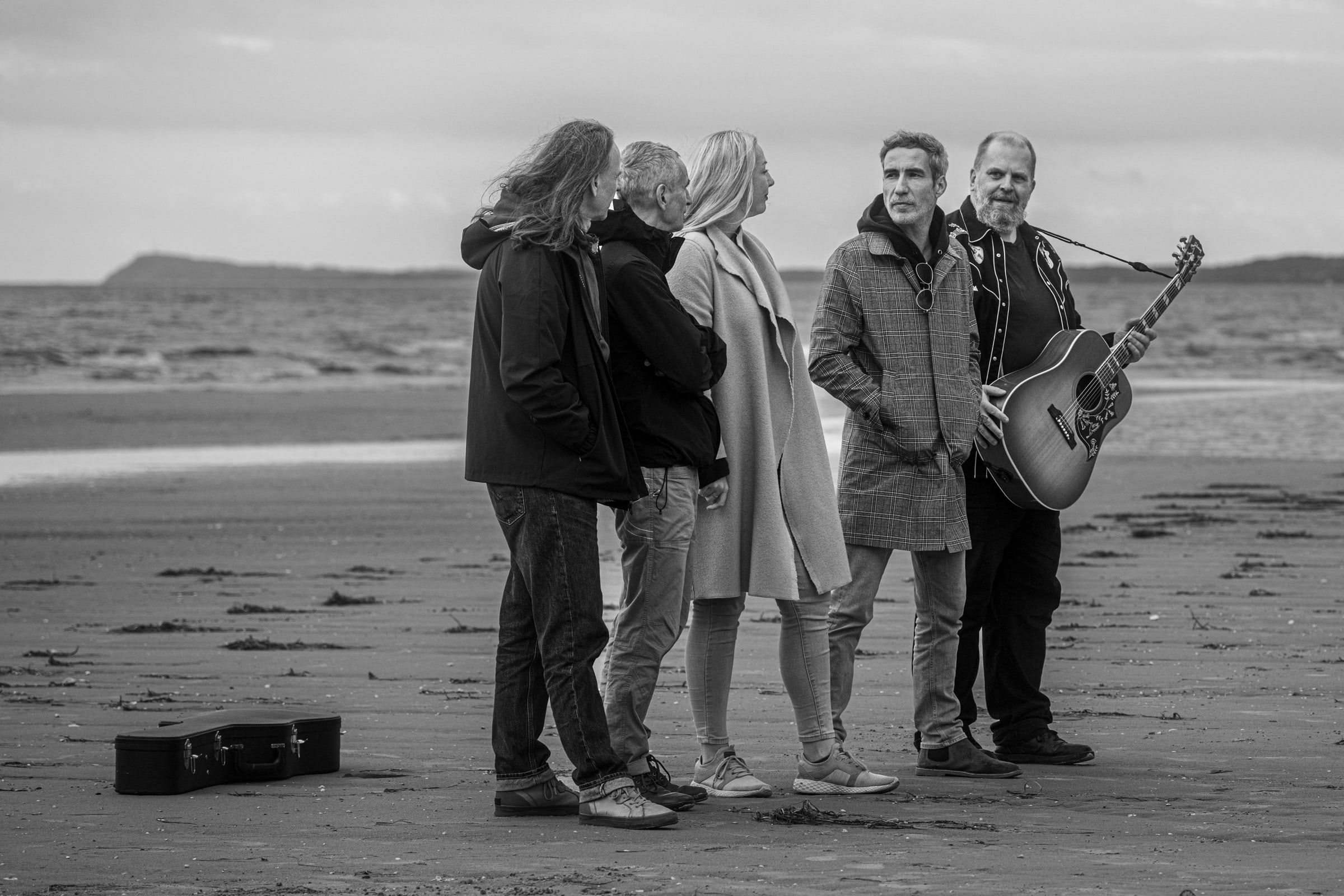 Die Band am Strand im Gespräch, einer hält eine Gitarre