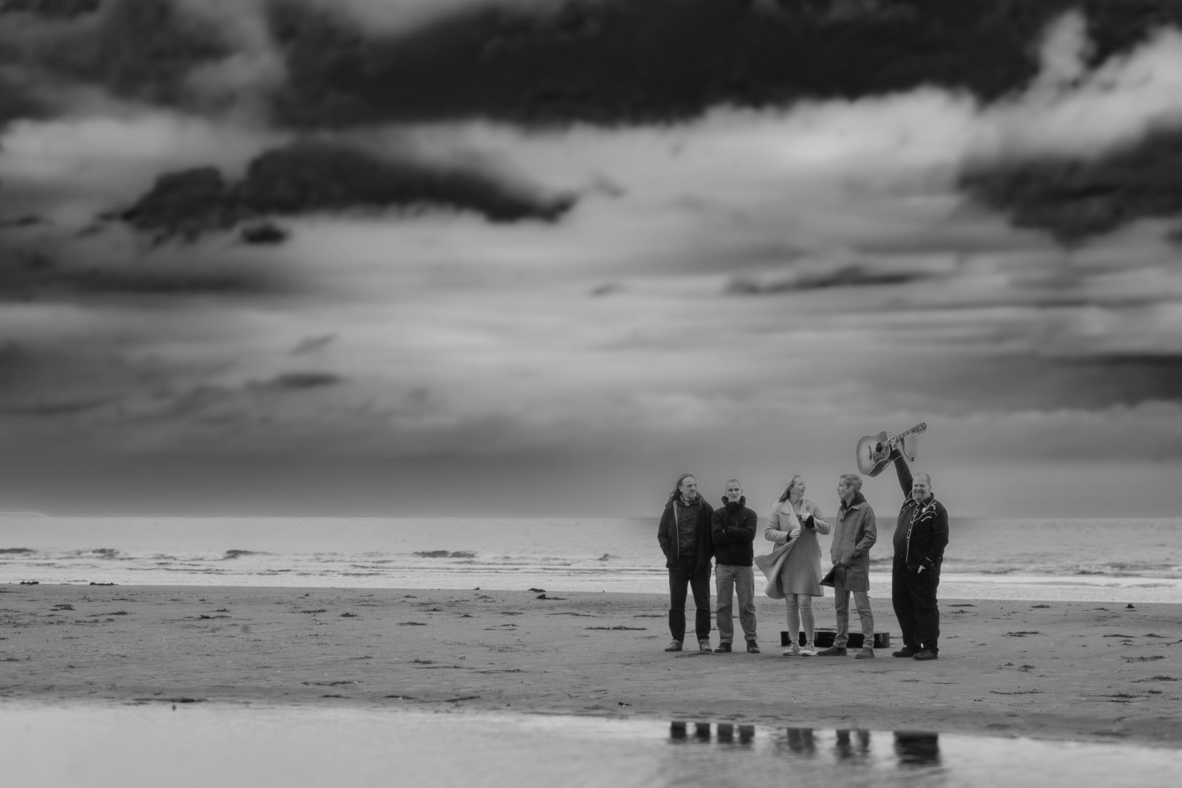 Die fünf von KARO NERO stehen klein und weit entfernt an einem flachen Ostseestrand unter grauem Himmel